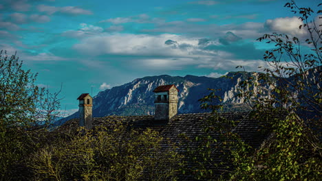 Blick-über-Das-Dach-Eines-Gebäudes,-Im-Hintergrund-Die-Alpen-Mit-Vorbeiziehenden-Wolken