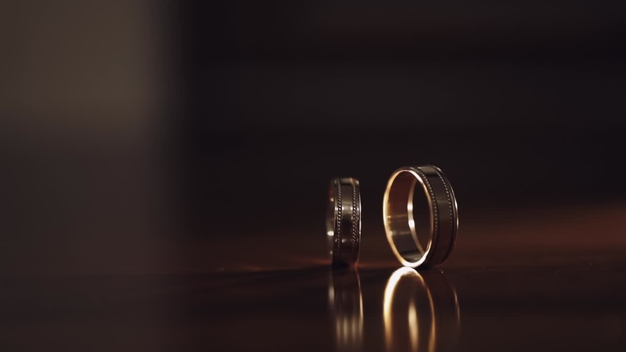 Close-up of turning spinning rotating wedding rings of groom and bride on table, marriage symbols