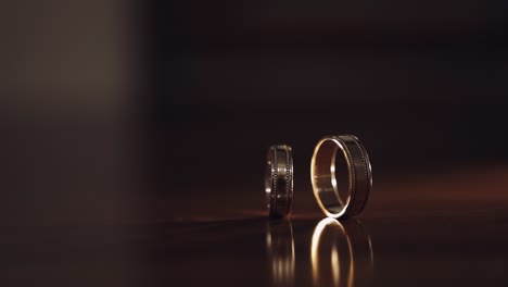 Close-up-of-turning-spinning-rotating-wedding-rings-of-groom-and-bride-on-table,-marriage-symbols