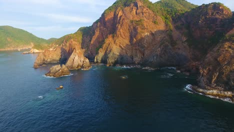 Volando-Bajo-Sobre-El-Agua-A-Lo-Largo-De-Los-Acantilados-Rocosos-En-El-Fondeadero-Carrizal-Cerca-De-Manzanillo,-México,-Justo-Antes-Del-Atardecer