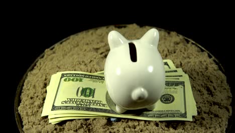 una alcancía blanca y billetes de un dólar giran sobre un fondo negro.