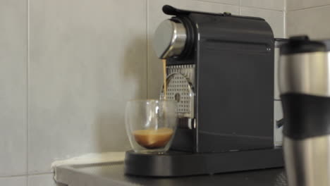 espresso coffee made from a machine into a transparent glass cup before being picked up by a man wearing a white shirt