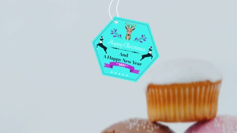 animation of christmas greetings on tag over cupcakes on white background