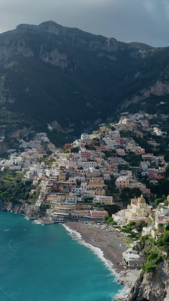 Panoramica aerea verticale e suggestiva della famosa Costiera Amalfitana di Positano con case a picco sulla scogliera, mare blu e paesaggio montano. Località turistica più popolare in Italia