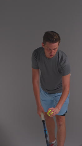 vertical video studio shot of male tennis player serving in match hitting ball with racket against grey background