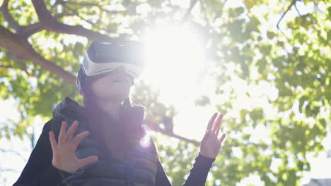 amazed young dark-haired woman in warm black waistcoat wearing virtual reality glasses in early autumn park