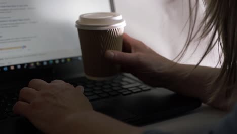 Busy-woman-working-on-a-laptop-in-office-with-takeout-coffee-close-up-shot