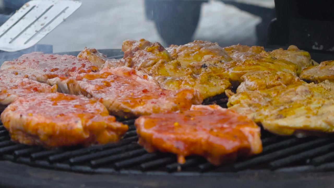 Riprese ravvicinate di carne cruda o manzo, pollo che viene posizionata su una griglia calda con le pinze al rallentatore mentre la griglia fuma. La carne è condita e ha della salsa, con buone ombre. A fuoco.