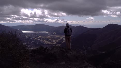 male hiker in winter clothing standing on top of mountain, looking down on plateau