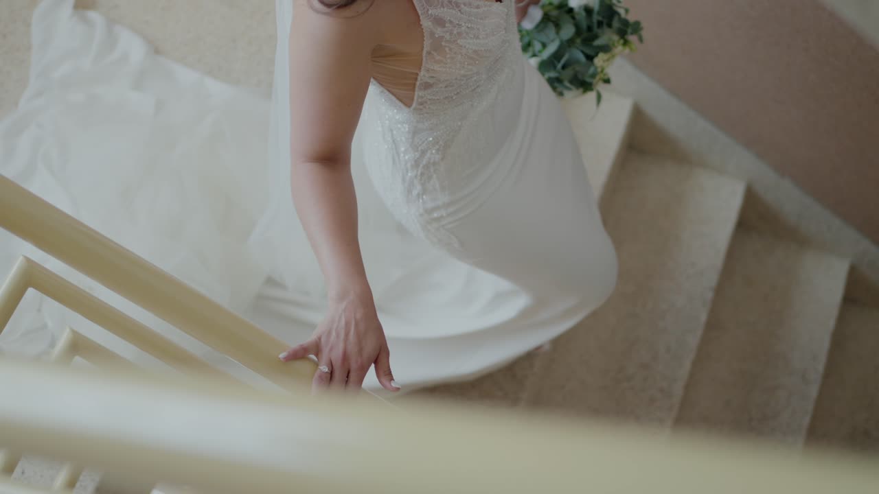 신부가 계단을 올라, 드레일을 들고, 그녀의 우아한 웨딩 드레스를 보여주고