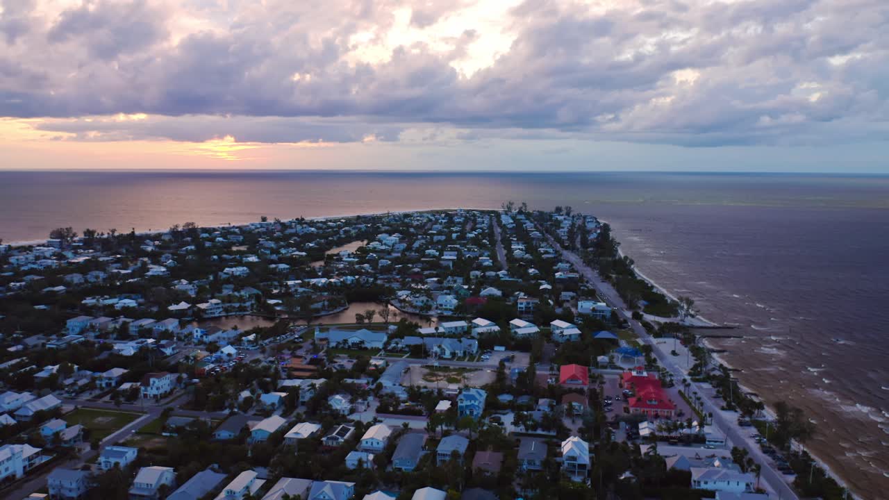 The sun sets over Anna Maria Island, casting a warm glow across the Gulf and the island’s patchwork of coastal homes beneath drifting evening clouds