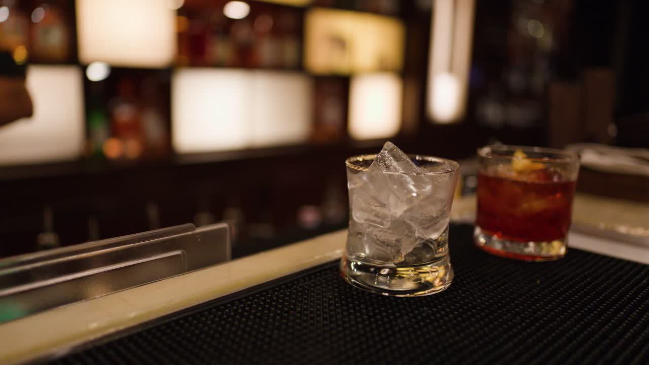 Bartender prepares whiskey cocktails with ice in dimly lit Bangkok bar, shallow depth of field