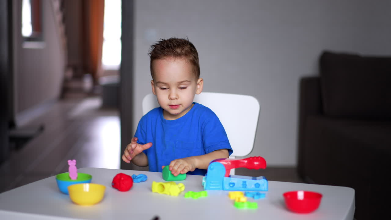 Beautiful little boy rolls the piece of plasticine by the desk. Creativity, art and game concept.