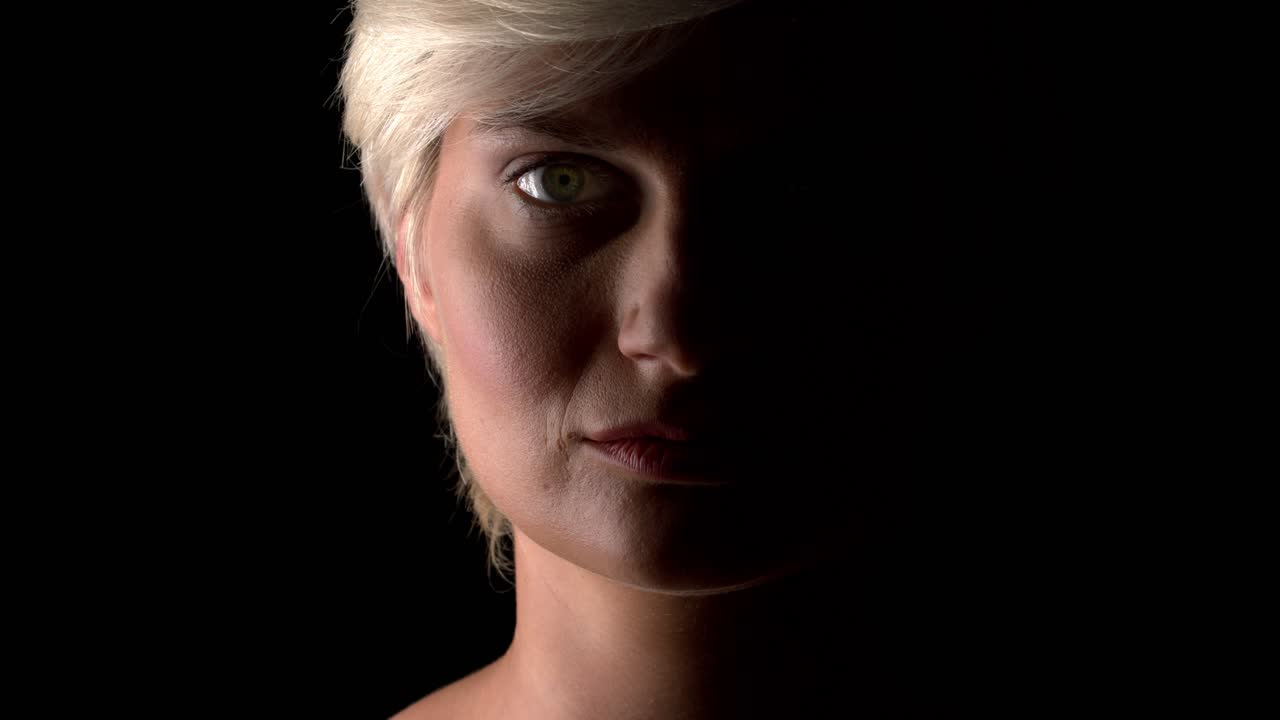 A close up of a lady's face, that is half covered by shadows, on a seamless studio background