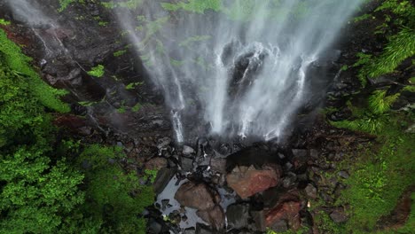 Descending-down-a-tropical-rainforest-waterfall-to-a-natural-rock-pool-below