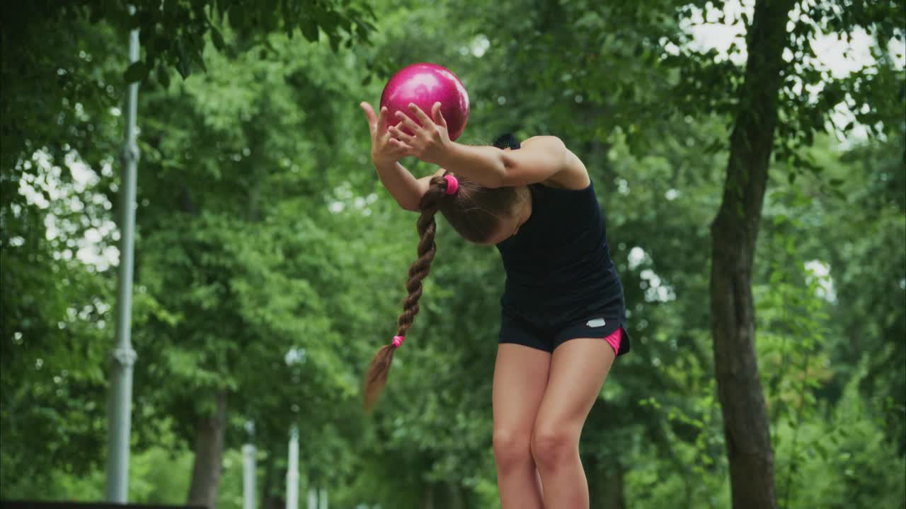 A Young Athlete Perfects Her Technique in a Serene Outdoor Environment, Balancing a Bright Pink Ball as She Prepares for Her Next Move or Challenge