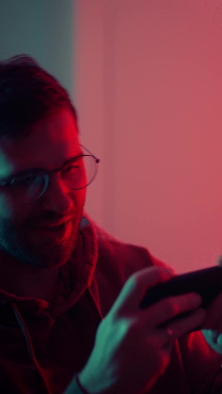 Begeistret ung mann som spiller mobilspill under neonlys