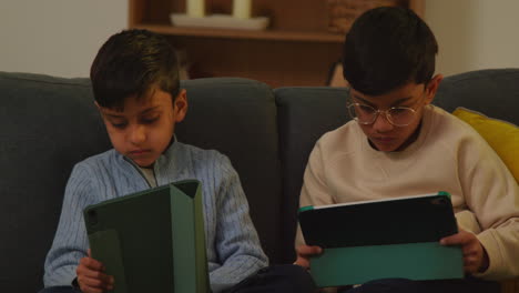 two young boys sitting on sofa at home playing games or streaming onto digital tablets 1