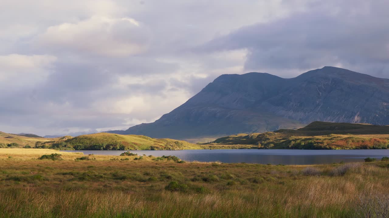 Shadows from drifting clouds move across the mountains and moorland at Loch Stack in the Scottish Highlands, creating dramatic light over the rugged landscape