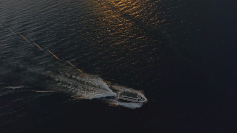 Toma-Aérea-De-Un-Barco-Grande-Que-Se-Mueve-A-Alta-Velocidad-A-Través-Del-Lago-Di-Garda-En-Una-Cálida-Y-Suave-Luz-Del-Atardecer