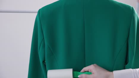 woman using lint roller on back side of green suit at laundry shop