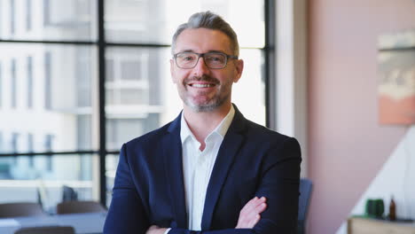 portrait of smiling mature businessman wearing glasses  standing in empty office