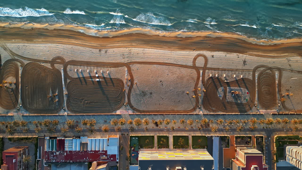 Aerial drone view of palm trees on a promenade near the beach and buildings along coastline of the city in Alicante, Spain at sunset