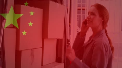 Animación-De-La-Bandera-China-Ondeando-Sobre-Una-Mujer-Usando-Un-Teléfono-Inteligente-Junto-A-Cajas-De-Cartón.