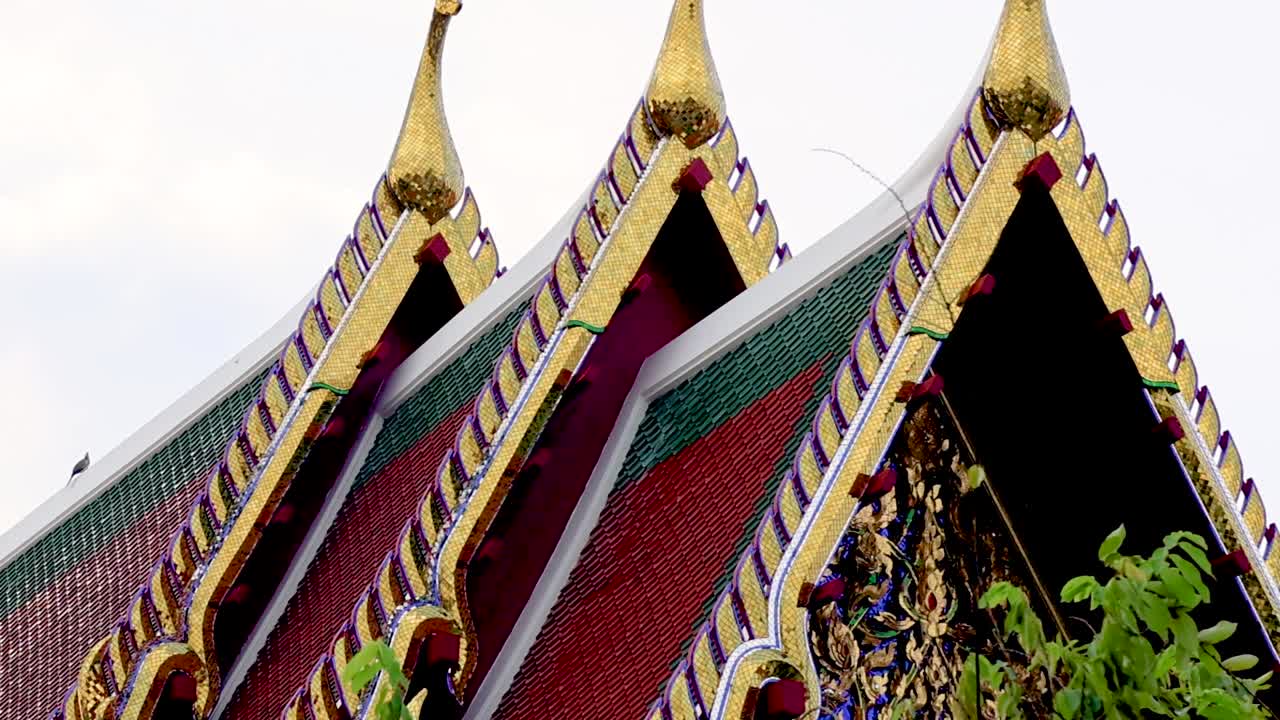 Close-up view of ornate gable roofs adorned with gold and surrounded by vibrant green foliage.