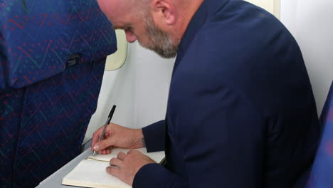 a man writing in a diary notebook journal on a passenger plane airliner