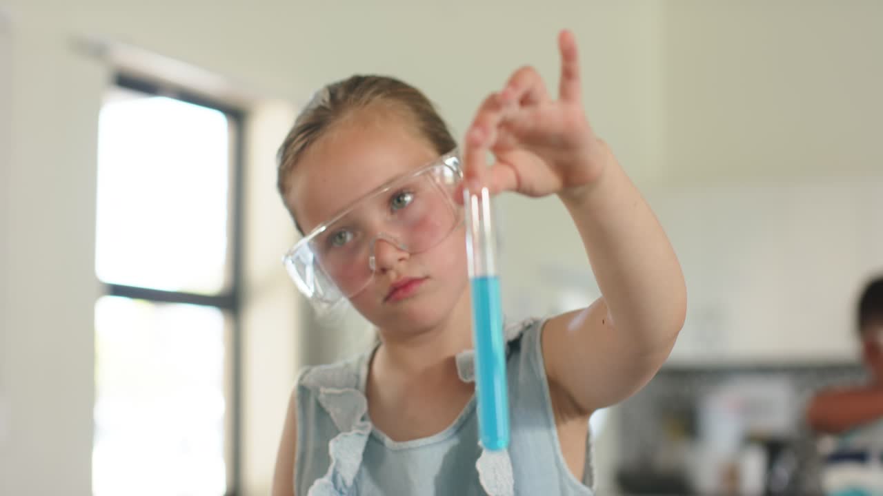 Alunna con occhiali protettivi che si protende verso la rastrelliera, selezionando e ispezionando un liquido blu per il laboratorio di scienze