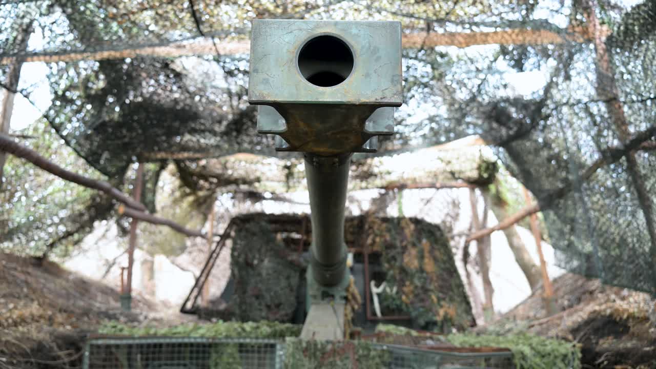 A powerful close-up shot looking directly down the barrel of a PzH 2000 howitzer. The German-made artillery is hidden under camouflage netting on the Ukrainian front