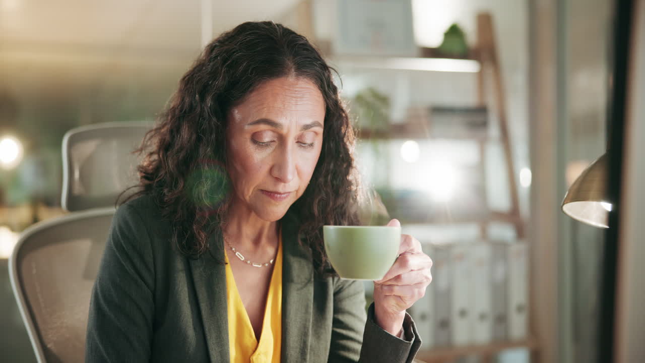 사무실에서 노트북을 쓰고 웃으며 커피를 마시고 있는 사업가입니다.