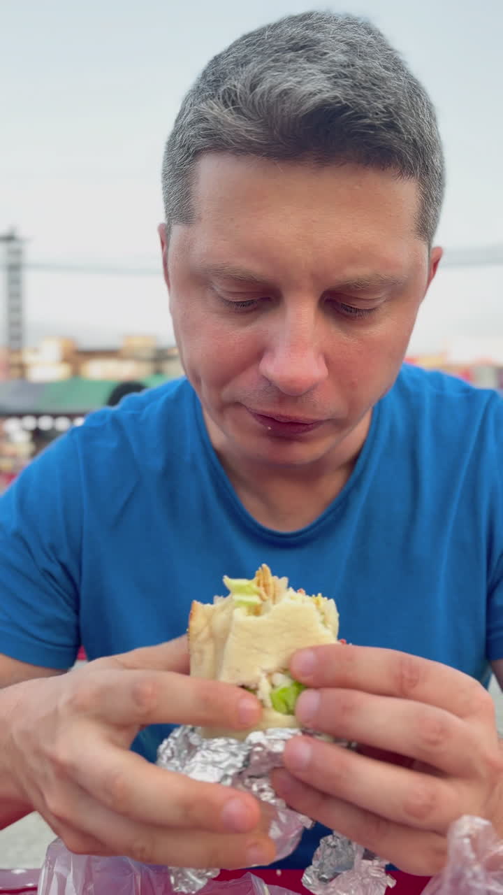 Close-up de homem a comer um wrap de kebab ao ar livre. Cena de refeição fast food de rua, adequada para publicidade alimentar, conteúdo de estilo de vida e conceitos de refeição informal.