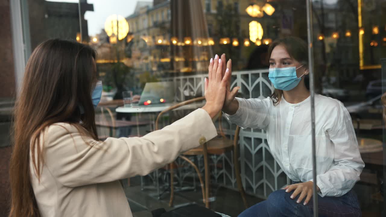 друзья встречаются через окно кафе с масками на лице