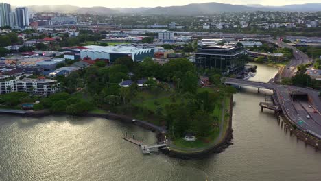 vista panorámica aérea cinematográfica a lo largo de la orilla norte del río capturando el arroyo del desayuno y el complejo de apartamentos residencial frente al mar en el suburbio del centro de la ciudad de newstead al atardecer, brisbane, queensland