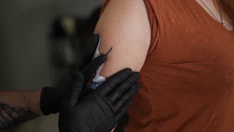 the tattoo artist applies the sketch on the woman's skin of upper hand. trying to fit the colorful sketch on female unrecognizable client, hold it, waits until it sticks. close up