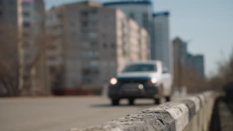 close view of an urban road with a car in motion in the background, it focus on the weathered road barrier, with the blurred cityscape and vehicles passing by