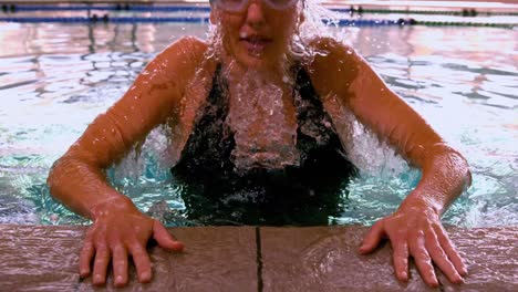 fit swimmer emerging from pool and pulling herself up