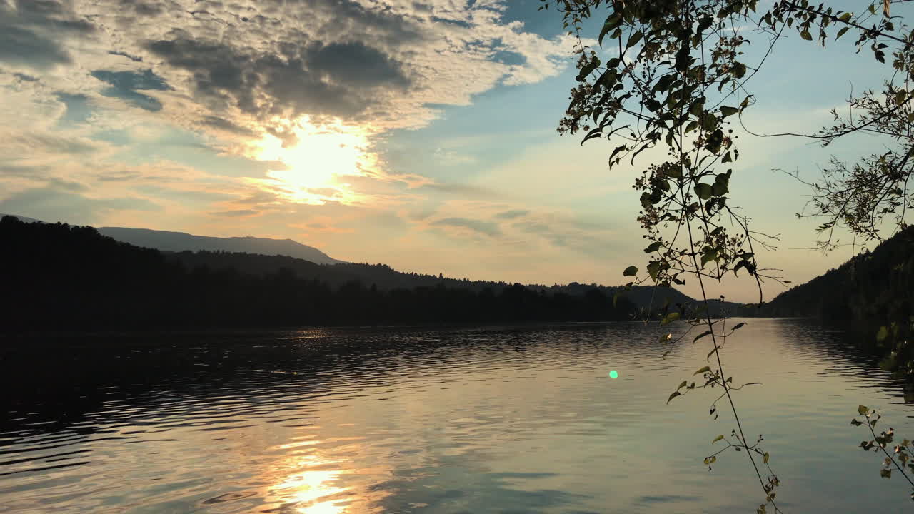 hermoso lago con siluetas de árboles y una puesta de sol dorada en un cielo nublado