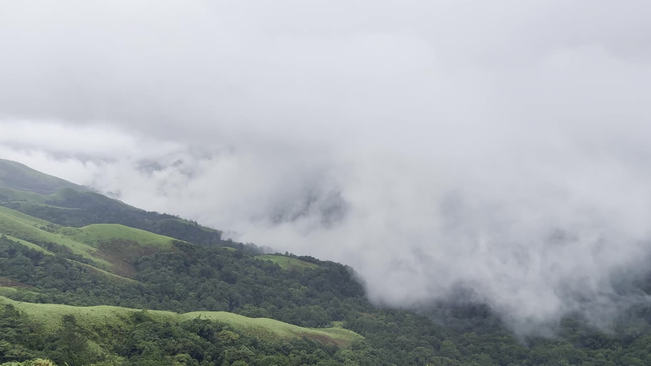 Rolling green mountains of Devarmane, Malnad, Karnataka during monsoon. Rain clouds sweep swiftly overhead, capturing the serene and dramatic beauty of the Western Ghats