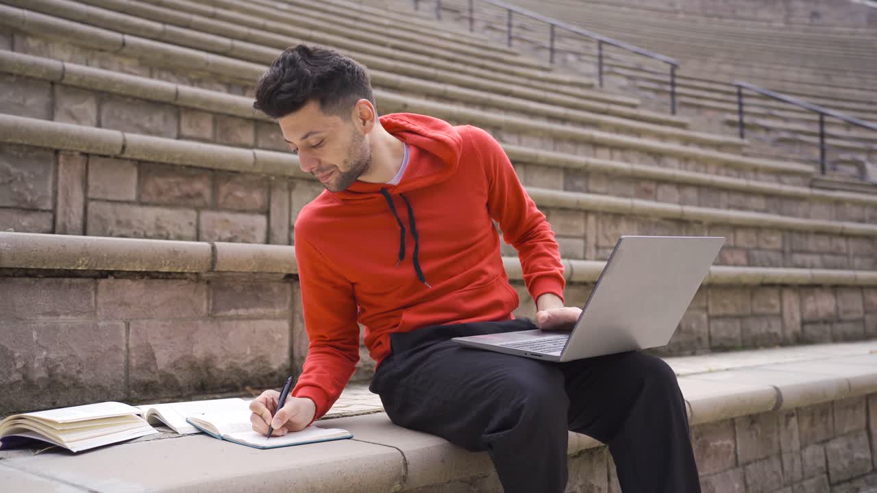 Young adult male student studying in the park using laptop.