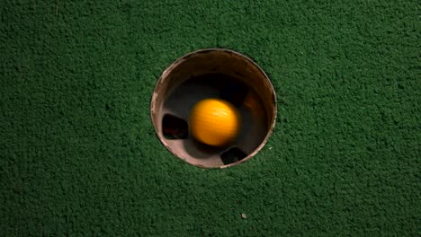 a close up birds eye view of a yellow mini golf ball falls into the golf hole and bounces in the pocket on a course