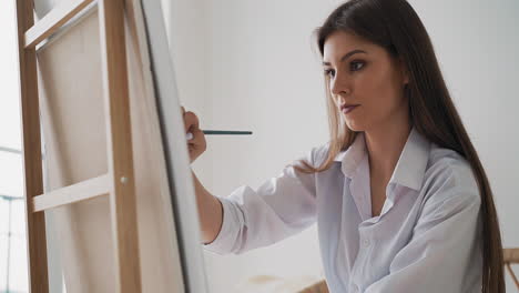 una mujer de pelo largo dibuja una imagen en un lienzo en un estudio de arte ligero