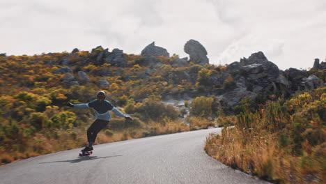 happy young man riding longboard skating fast enjoying competitive race cruising downhill on countryside road doing tricks using skateboard wearing helmet