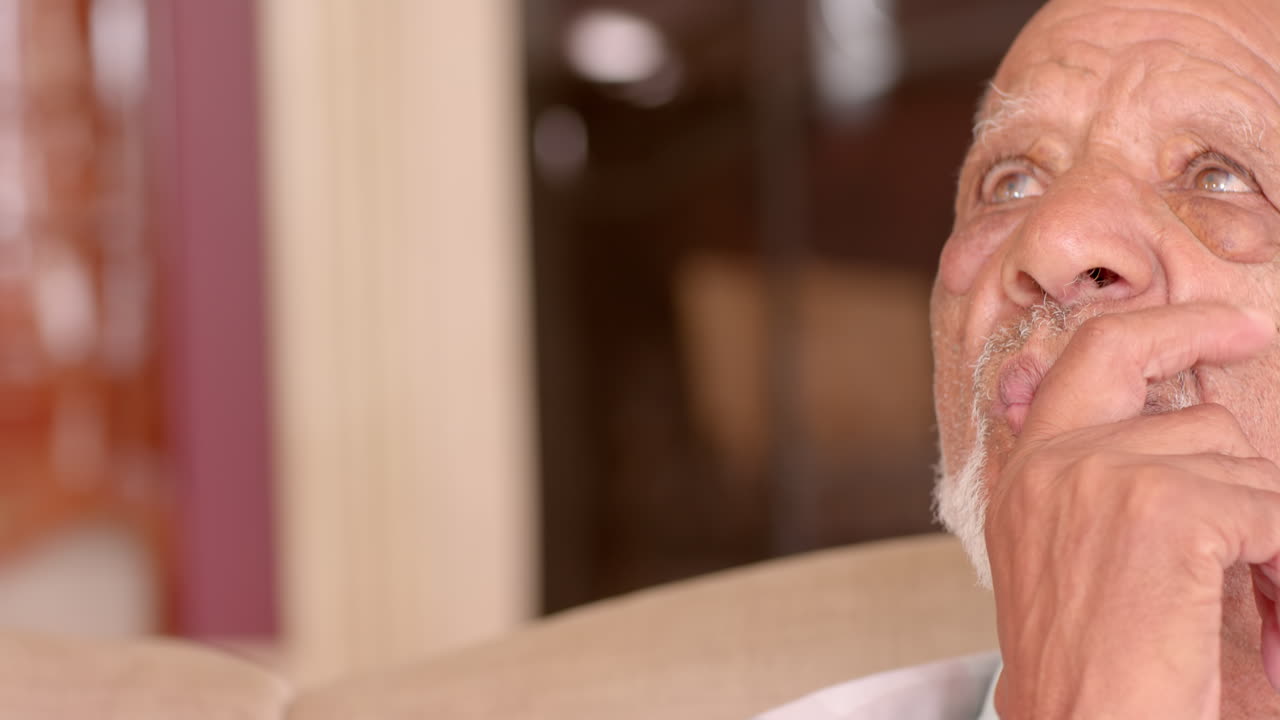 Sitting at home, elderly man gazing thoughtfully into distance, copy space