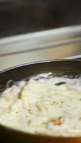 cooking delicious meal in white sauce. chef is cooking tasty dish in a frying pan in a restaurant. close-up. vertical video