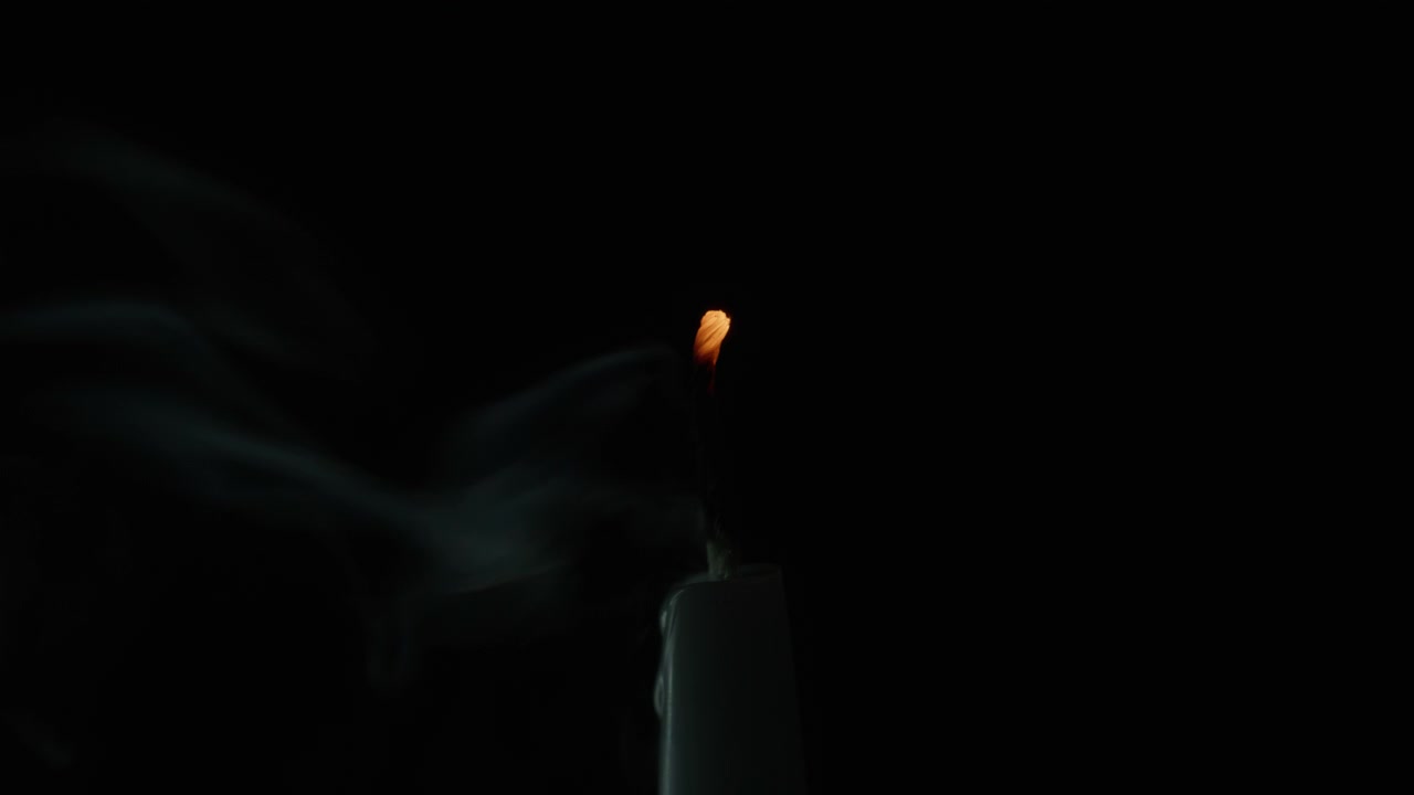 Primo piano di una brezza che spegne la fiamma di una candela, vista scura. Fine della fiamma della candela di cera, nero