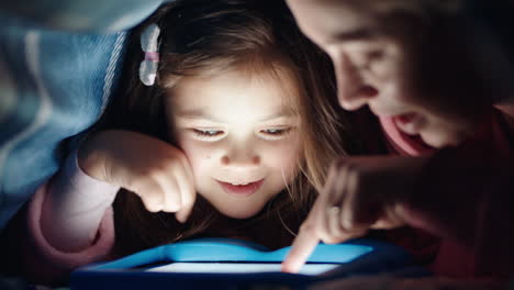 Feliz-Madre-E-Hija-Usando-Una-Tableta-Bajo-Una-Manta-Jugando-Juegos-En-Tecnología-De-Pantalla-Táctil-Relajándose-Divirtiéndose-Antes-De-Acostarse