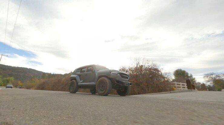 Ripresa FPV di un'auto fuoristrada futuristica che guida su strada rurale sotto un cielo azzurro